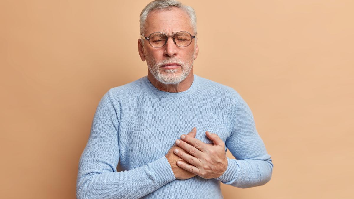 grey-haired-displeased-bearded-old-man-has-sudden-painful-spasm-chest-closes-eyes-presses-hands-heart-poses-against-beige-wall_93242100