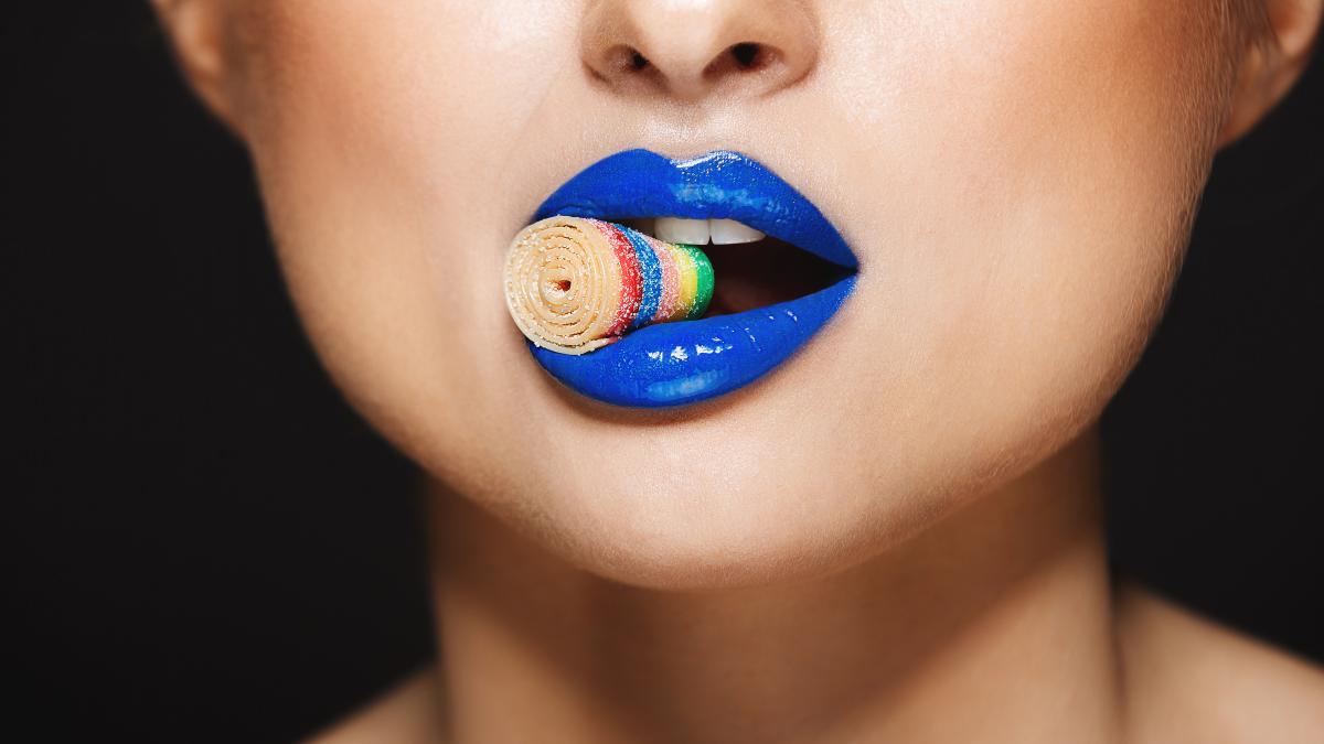 sexy-colorful-lips-holding-sweeties-with-teeth-grey-wall_80456000