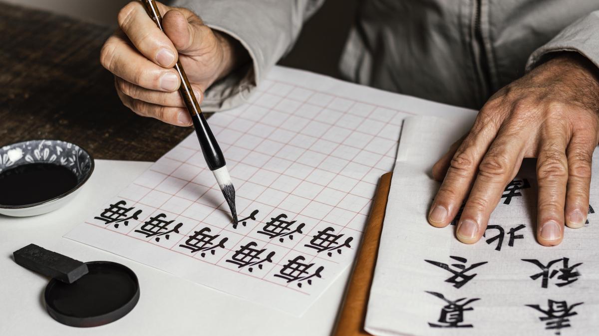 high-angle-person-writing-chinese-symbols-white-paper_38570700