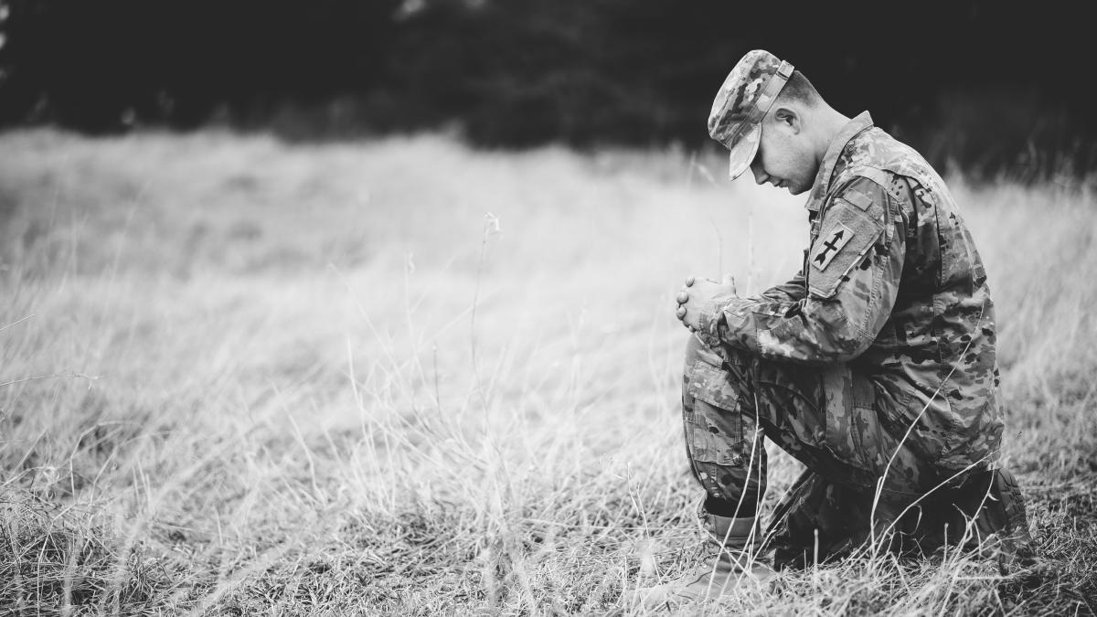 grayscale-shot-young-soldier-praying-while-kneeling-dry-grass_18051100
