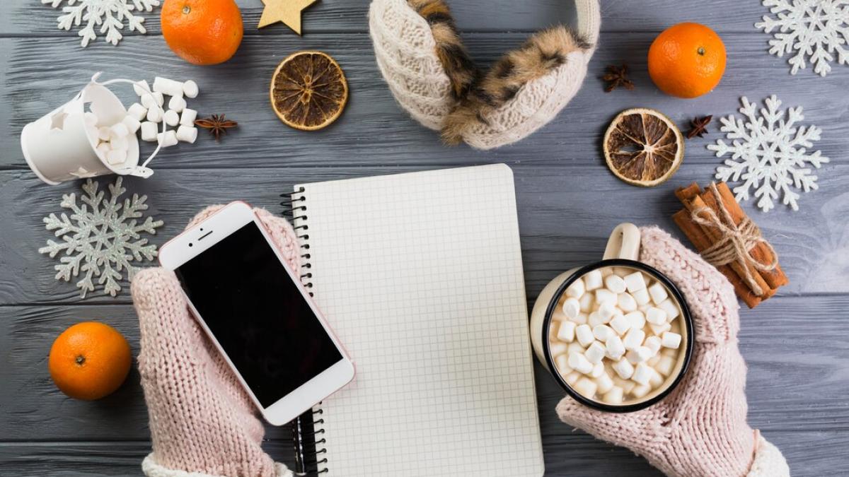 hands-mittens-with-smartphone-cup-with-marshmallow-near-notebook-paper-snowflakes_23-2147987589_88632300
