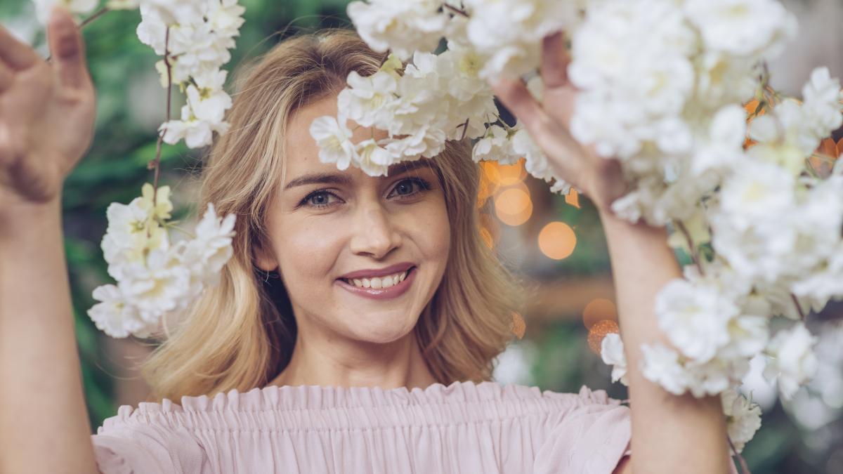 close-up-smiling-young-woman-looking-through-white-flowers_49610800