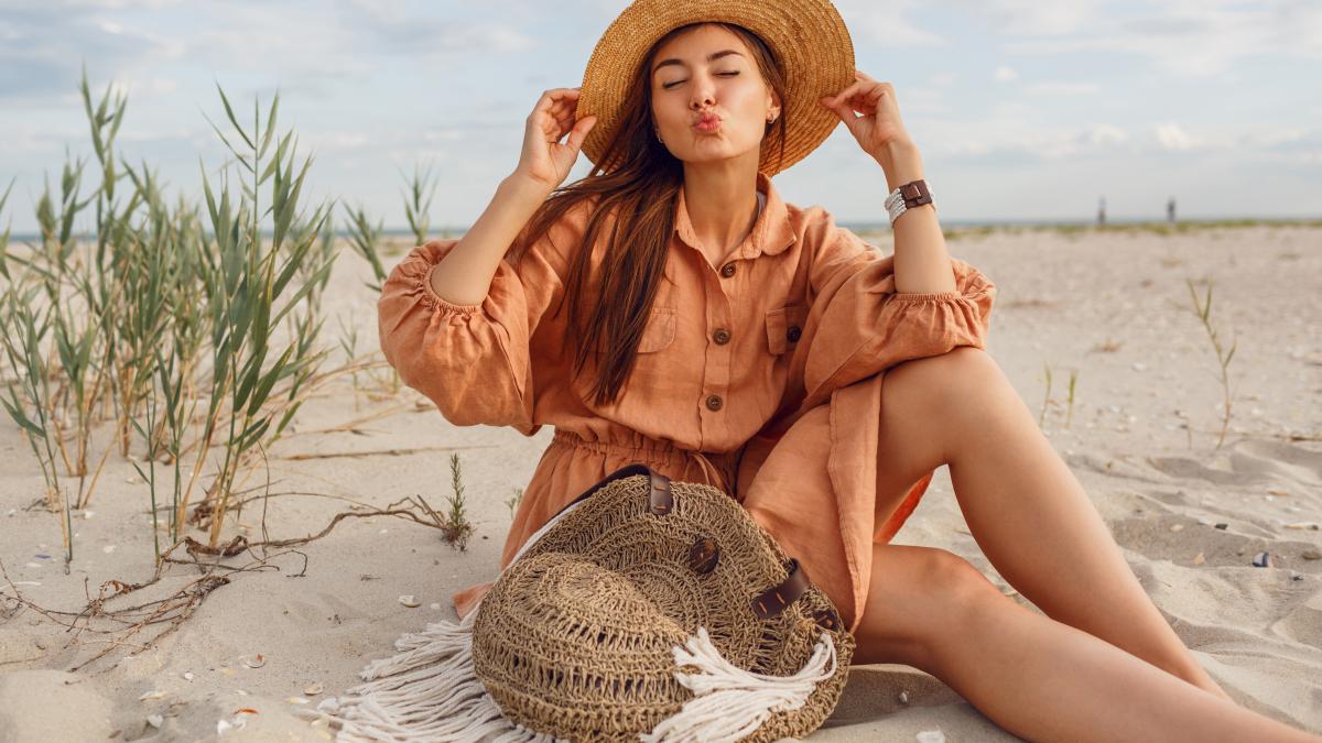 cute-brunette-girl-send-kiss-relaxing-beach-wearing-summer-fashionable-linen-clothes-straw-hat-boho-bag_07577800
