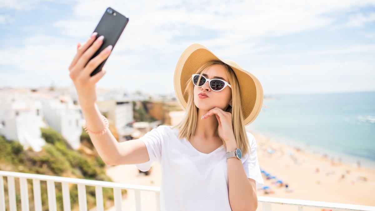 pleasant-girl-sunglasses-hat-touching-her-cheek-while-making-selfie-sea_52255500