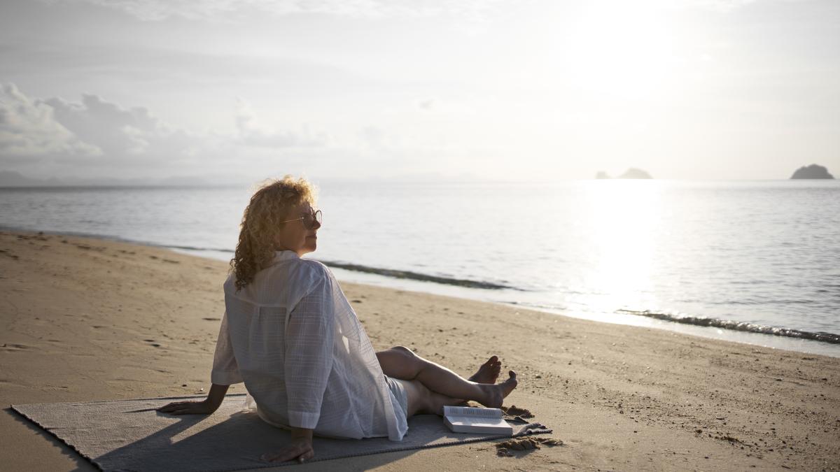 side-view-woman-sitting-beach-with-book_91366400