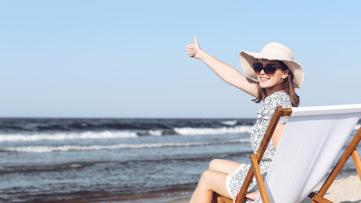 happy-brunette-woman-sitting-wooden-deck-chair-ocean-beach-while-showing-thumb-up_60114600