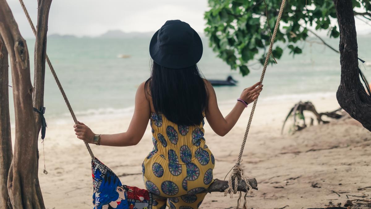 rear-view-woman-sitting-swing-beach_86034700