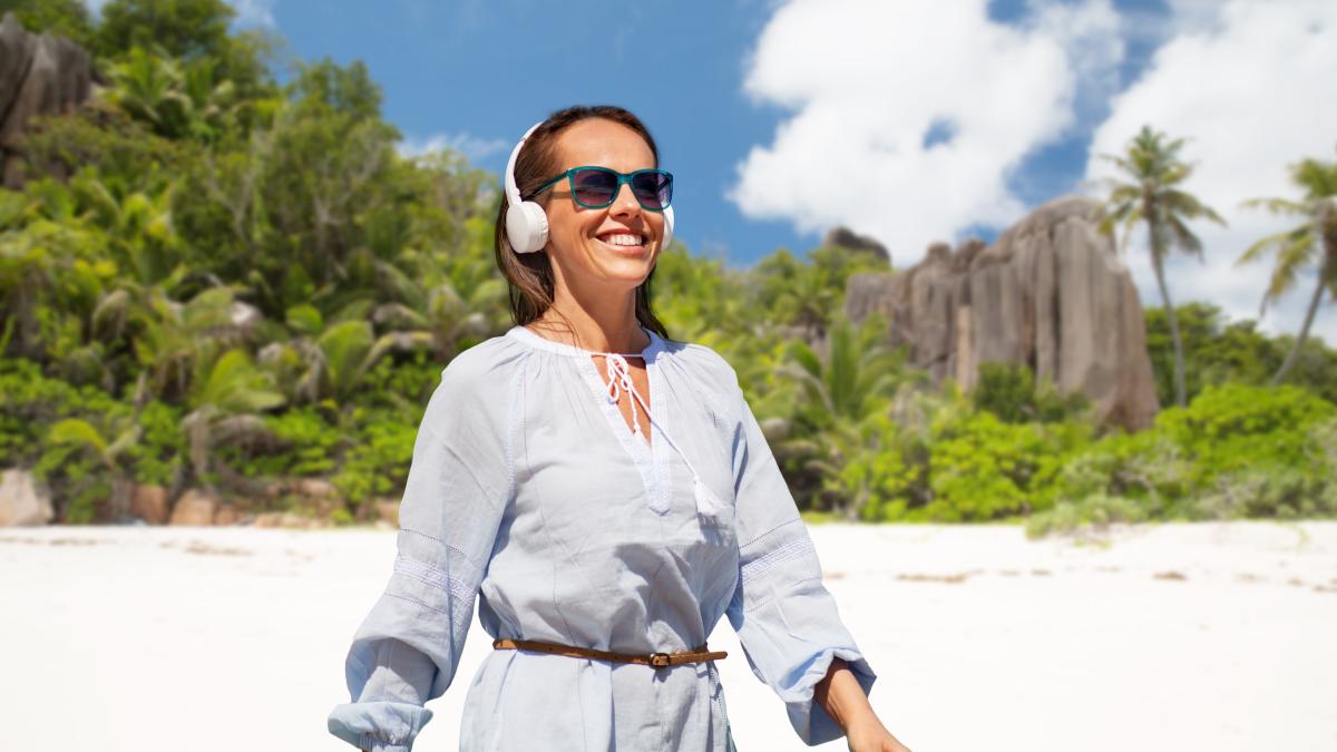 woman-with-headphones-walking-along-summer-beach_92555800